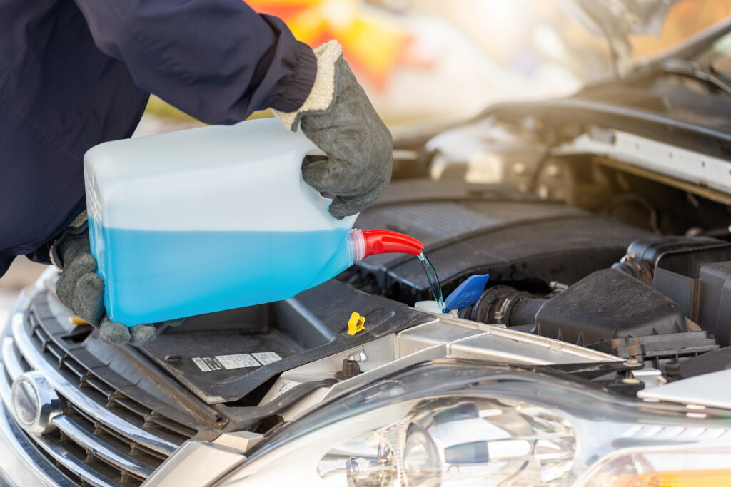 Person pouring antifreeze to the car in wintertime. Technician with open hood adding cooland to the motor in winter. Human hand with bottle of blue liquid.